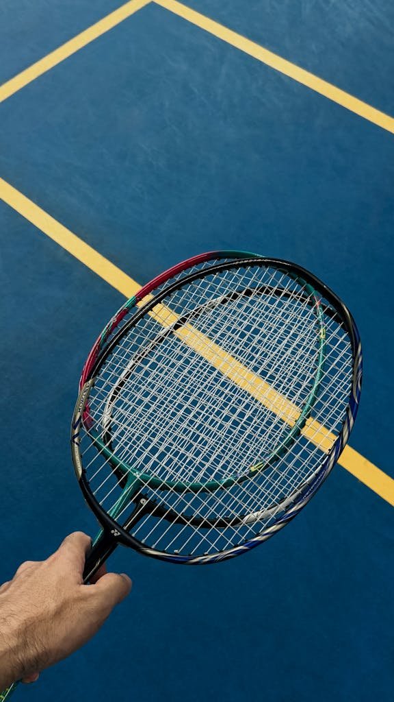 Close-up of a hand holding a badminton racket on a blue court in Ho Chi Minh City.