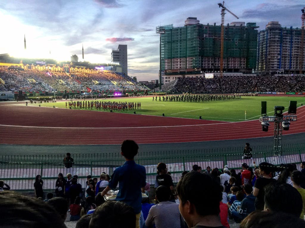 Crowd enjoying a lively sports event at a Cambodian stadium in the evening.