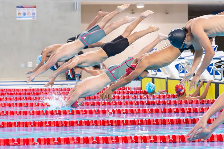 Swimmers dive into the pool during a competitive race in an indoor facility.